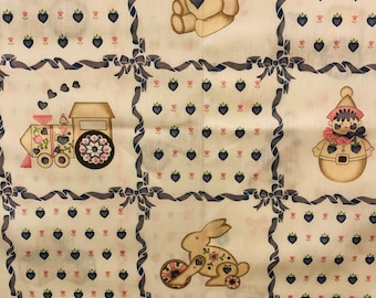 May include: A white fabric with a repeating pattern of blue and pink hearts, a train, a bunny, a teddy bear, and a gingerbread person. The fabric is framed by a blue ribbon with bows.