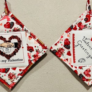 May include: Two red and white quilted pot holders with Valentine's Day themes. One pot holder features a heart wreath with the text "To my Valentine". The other pot holder features a red heart with the text "Valentine Greetings".