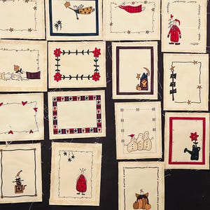 Könnte beinhalten: Eine Sammlung kleiner, rechteckiger, handgemalter Kunstwerke. Jedes Stück hat einen cremefarbenen Hintergrund, einen dekorativen Rahmen und eine zentrale Illustration. Die Illustrationen umfassen Sterne, Figuren und saisonale Motive. Die Rahmen sind in verschiedenen Farben.