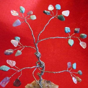 May include: A wire tree sculpture with various colored gemstones attached to the branches. The tree is sitting on a white rock base.