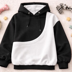 May include: A black and white color block hoodie with a drawstring hood. The hoodie has a unique curved design on the front and is surrounded by dog toys and star-shaped decorations.