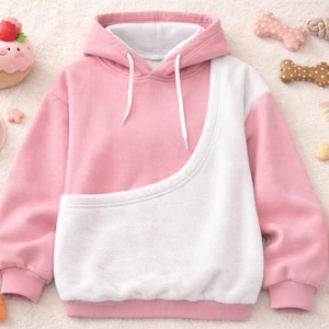 May include: Pink and white pet carrier hoodie with a kangaroo pouch. The hoodie is surrounded by pet toys, including a plush carrot, strawberry, and a bowl of pet food. The hoodie has a drawstring hood.