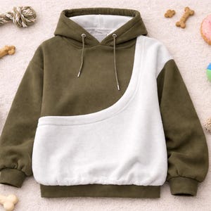 May include: Olive green and white pet carrier hoodie with a drawstring hood. The image includes dog toys, a bowl of kibble, and a stuffed lamb. The hoodie has a large white pocket for carrying a pet.