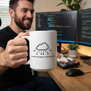 May include: White ceramic mug featuring a black cloud and circuit design, with the text "I make changes in production." The mug is held by a person in front of a computer setup.