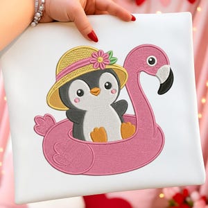 May include: Embroidered design of a penguin wearing a straw hat with a pink flower, floating on a pink flamingo float. The penguin has a white belly, black wings, and orange feet. The flamingo float has a black beak.