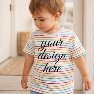 May include: A short-sleeved, striped t-shirt with the text "your design here" in black script. The shirt features horizontal stripes in various colors, including red, yellow, green, and blue. The child is wearing blue jeans.