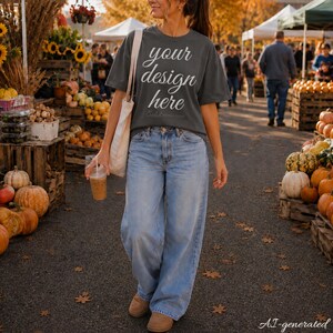 May include: A charcoal gray short-sleeve t-shirt with the white text "your design here" printed on the front, paired with light blue wide-leg denim jeans and a beige canvas tote bag, creating a casual outfit for an outdoor autumn setting.