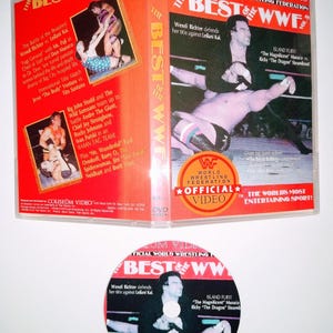 Könnte beinhalten: Eine DVD-Hülle und -Disc für "The Best of WWF" Wrestling. Die Hülle ist rot und weiß und zeigt Bilder von Wrestlern in Aktion. Die Disc hat ein ähnliches Design mit dem Titel und Bildern von Wrestlern. Der Text auf der Hülle enthält "Official Video".