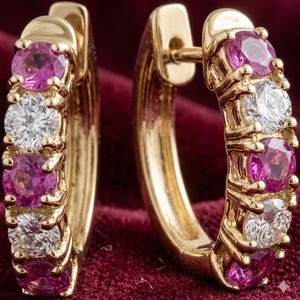 Peut inclure: Une paire de boucles d'oreilles créoles en or avec des pierres roses et des diamants transparents alternés. Les boucles d'oreilles sont posées sur un tissu de velours rouge, mettant en valeur leur éclat. Les pierres sont taillées rondes.