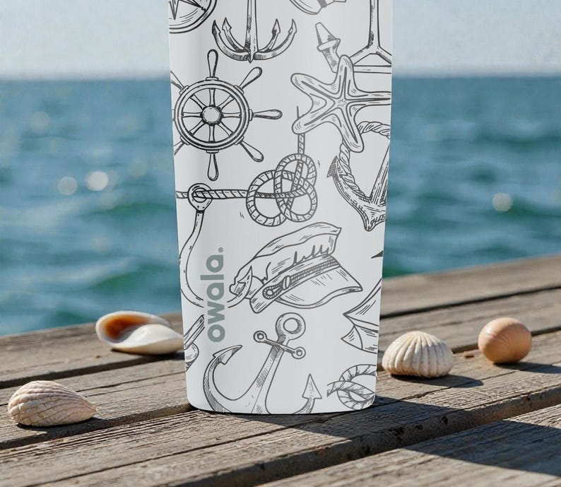 May include: White water bottle with a nautical-themed pattern of anchors, ship wheels, and rope knots. The bottle has the word "owala." printed on it. The background features a wooden dock, seashells, and the ocean.