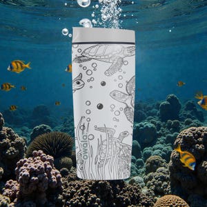 以下が含まれることがあります： グレーの蓋が付いた白いトラベルタンブラー。ウミガメ、魚、水生植物の白黒イラストが描かれています。タンブラーの側面にはブランド名「owala」がプリントされています。背景には、サンゴと魚がいる水中シーンが描かれています。