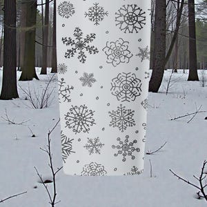 Puede incluir: Tela blanca con un patr&oacute;n repetido de copos de nieve grises en varios dise&ntilde;os. La tela cuelga en un entorno de bosque nevado, lo que sugiere un tema de invierno o festivo. Los copos de nieve son detallados y art&iacute;sticos.