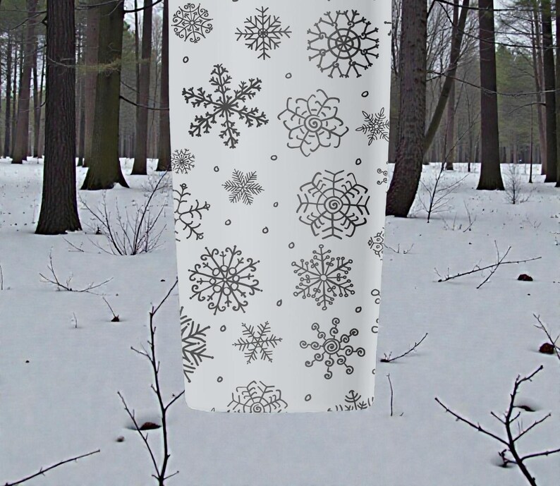 Puede incluir: Tela blanca con un patr&oacute;n repetido de copos de nieve grises en varios dise&ntilde;os. La tela cuelga en un entorno de bosque nevado, lo que sugiere un tema de invierno o festivo. Los copos de nieve son detallados y art&iacute;sticos.