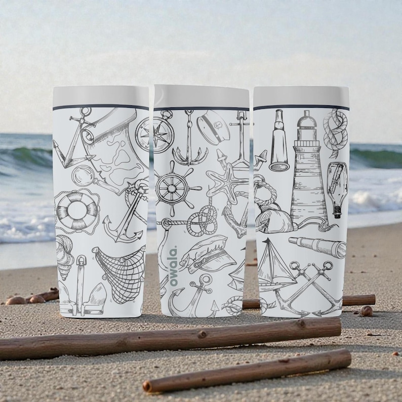 May include: Three white travel mugs with a nautical theme, featuring black line drawings of anchors, compasses, lighthouses, and sailboats. The mugs have a white lid and the brand name "owala" is visible on one of the mugs. The mugs are on a sandy beach.