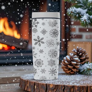 Puede incluir: Un termo blanco con tapa, decorado con patrones de copos de nieve negros. El termo es cil&iacute;ndrico y parece estar hecho de material aislante. El fondo incluye una chimenea, pi&ntilde;as y nieve, sugiriendo un tema invernal.