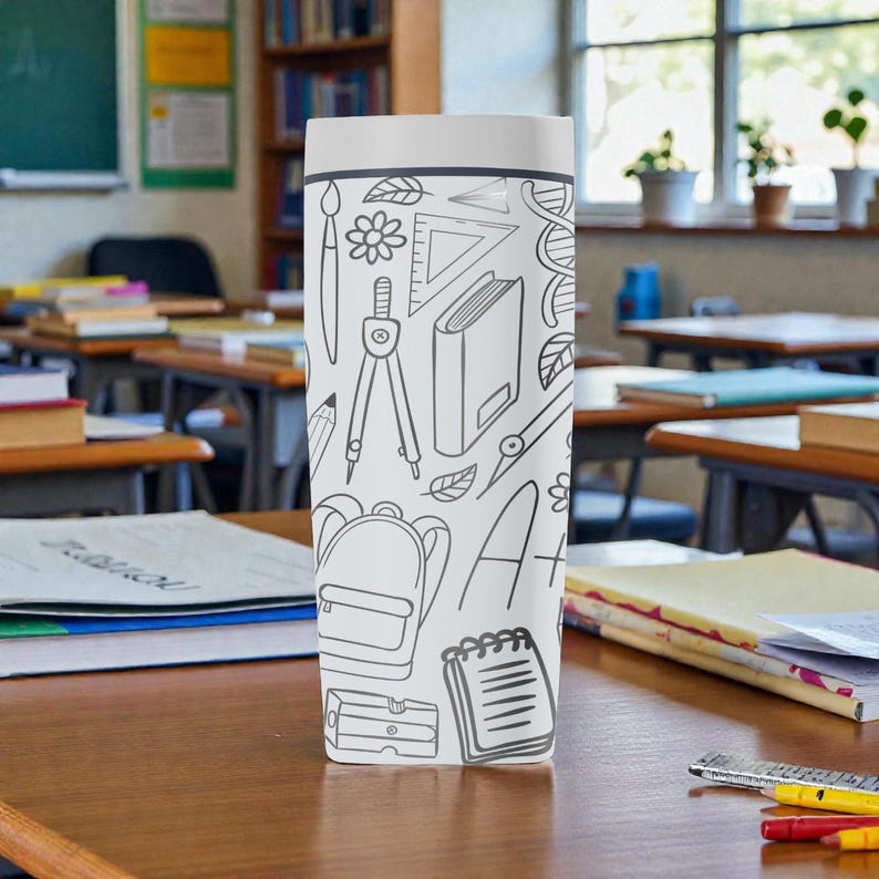 Op de afbeelding: Een wit en grijze reismok met een schoolthema-ontwerp. Het ontwerp bevat illustraties van een rugzak, passer, liniaal, potlood en andere schoolbenodigdheden. De mok is cilindrisch met een wit deksel.