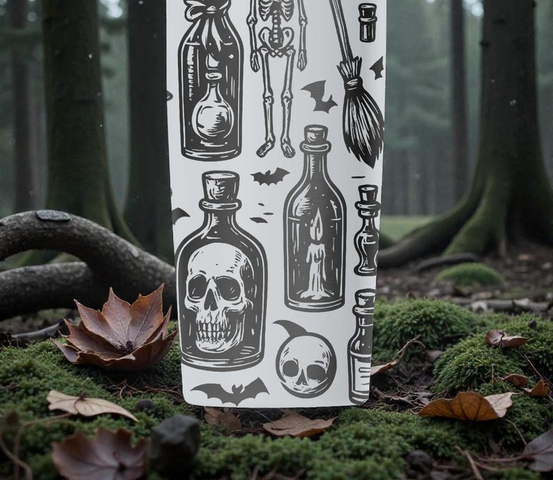 K&ouml;nnte beinhalten: Ein wei&szlig;er Becher mit einem schwarz-grauen Halloween-Design. Das Design umfasst Illustrationen von Zaubertr&auml;nken, einem Skelett, Flederm&auml;usen, einem Besen und einem Totenkopf. Der Becher steht vor einem Hintergrund aus Waldboden mit Moos und Herbstlaub.