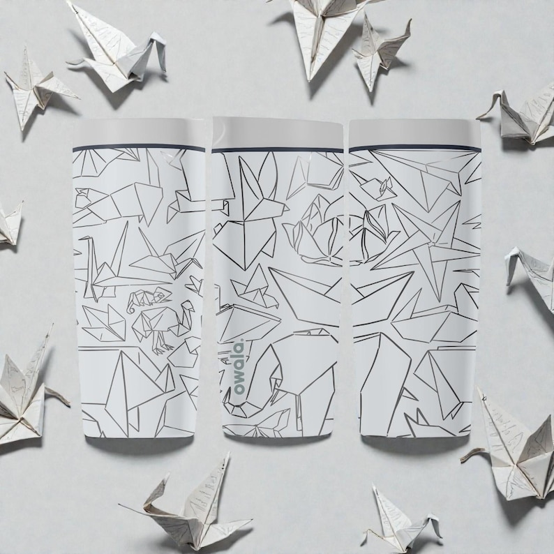 K&ouml;nnte beinhalten: Drei wei&szlig;e Owala-Wasserflaschen mit einem geometrischen Origami-Design in Schwarz. Die Flaschen sind von Origami-Papierkranichen umgeben. Die Flaschen haben einen wei&szlig;en Deckel und das Owala-Logo ist auf der Seite sichtbar.
