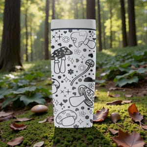 Peut inclure: Un gobelet de voyage blanc avec un motif de champignons noir et blanc. Le motif comprend diverses illustrations de champignons, des fleurs, des c&oelig;urs et des &eacute;toiles. Le gobelet est cylindrique et poss&egrave;de un couvercle blanc.