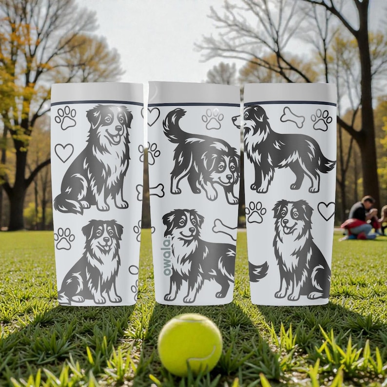 Puede incluir: Tres vasos aislados blancos con ilustraciones de perros negros, huellas de patas, corazones y huesos. Los vasos tienen un borde plateado y la palabra "owala" impresa en uno. Una pelota de tenis amarilla descansa sobre la hierba.