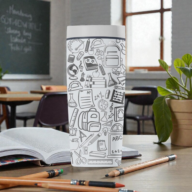 May include: A white tumbler with a black and white school-themed doodle pattern. The design includes images of backpacks, books, pencils, and mathematical symbols. The tumbler is on a wooden desk with pencils and an open book.