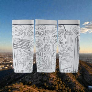 May include: Three white travel mugs with black line drawings of American landmarks and icons. The drawings include the Hollywood sign, the Statue of Liberty, an American flag, and a football jersey. The mugs have a white lid and a black band.