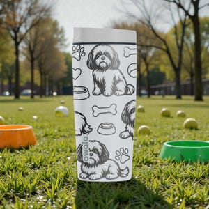 May include: A white Owala water bottle featuring a repeating pattern of a Shih Tzu dog, paw prints, hearts, dog bowls, and bones. The bottle is cylindrical with a white lid and is sitting on green grass.