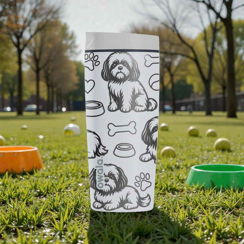 May include: A white Owala water bottle featuring a repeating pattern of a Shih Tzu dog, paw prints, hearts, dog bowls, and bones. The bottle is cylindrical with a white lid and is sitting on green grass.