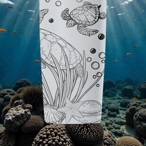 以下が含まれることがあります： 白いタンブラー。黒と白のイラストで、ウミガメ、泡、水生植物が描かれています。デザインにはヒトデと貝殻が含まれています。背景には、サンゴと魚がいる水中シーンが描かれています。