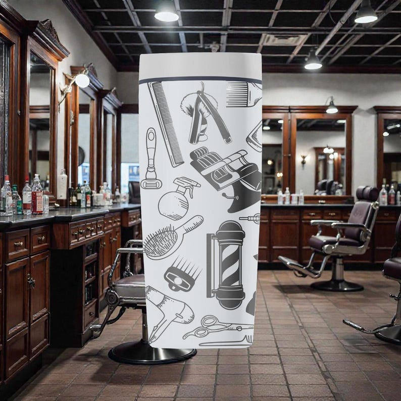 May include: A white, cylindrical banner featuring a repeating pattern of barber shop tools in black and gray. The design includes combs, razors, barber chairs, hair dryers, and scissors. The banner is displayed in a barber shop setting.