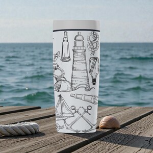 May include: A white travel mug featuring nautical-themed illustrations in black and white. Designs include a lighthouse, sailboat, anchor, rope knot, and a spyglass. The mug is cylindrical with a white lid, set against a wooden dock with the ocean in the background.