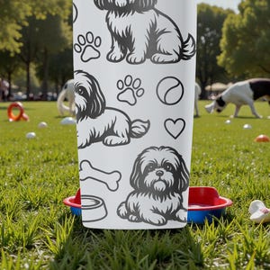 May include: White tumbler featuring black line art of Shih Tzu dogs, paw prints, a bone, a ball, and a heart. The tumbler is set in a park with dogs playing in the background. A red and blue dog bowl is in front of the tumbler.