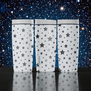 May include: Three white Owala tumblers with a pattern of various sized gray stars. The tumblers have a gray rim and the Owala logo is visible on one of the tumblers. The background is a starry night sky.