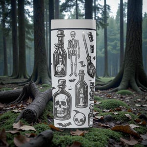 K&ouml;nnte beinhalten: Ein wei&szlig;er Becher mit schwarzen Illustrationen von Zaubertr&auml;nken, einem Skelett, einem Besen und Totenk&ouml;pfen. Der zylindrische Becher steht vor einem Waldhintergrund mit Moos und B&auml;umen. Das Design hat ein Halloween-Thema.