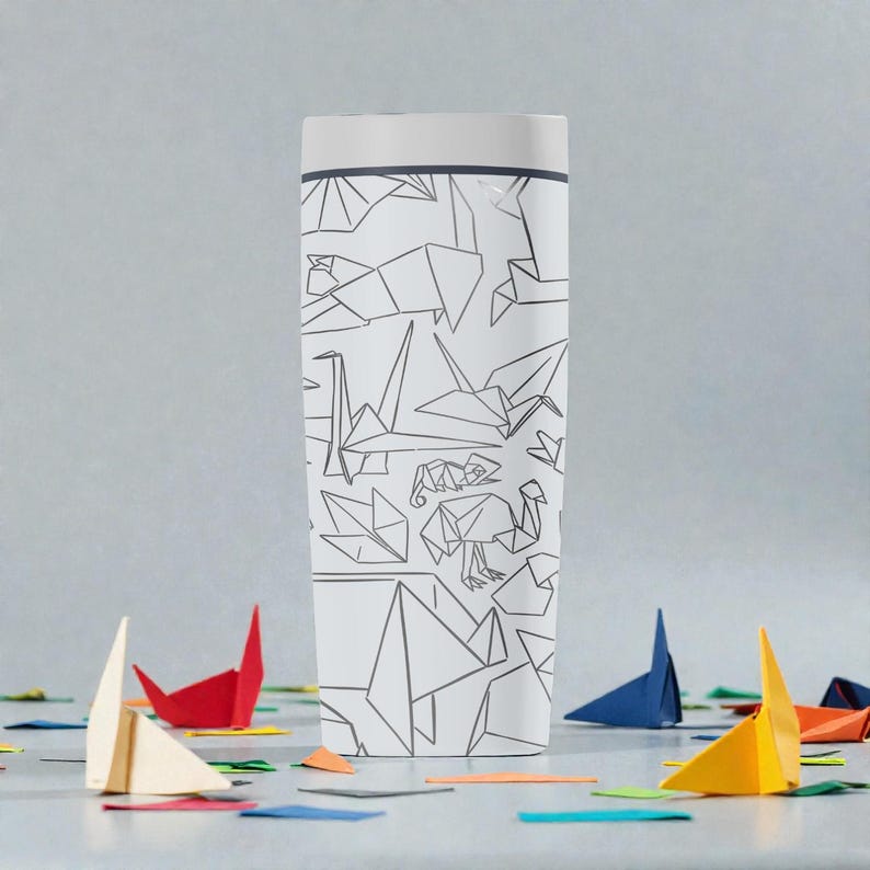 K&ouml;nnte beinhalten: Wei&szlig;er Reisebecher mit Deckel, verziert mit einem sich wiederholenden Muster aus grauen Origami-Tieren. Origami-Papierboote und bunte Papierschnipsel sind um die Basis des Bechers verstreut. Der Becher hat einen wei&szlig;en Deckel und einen grauen Rand.