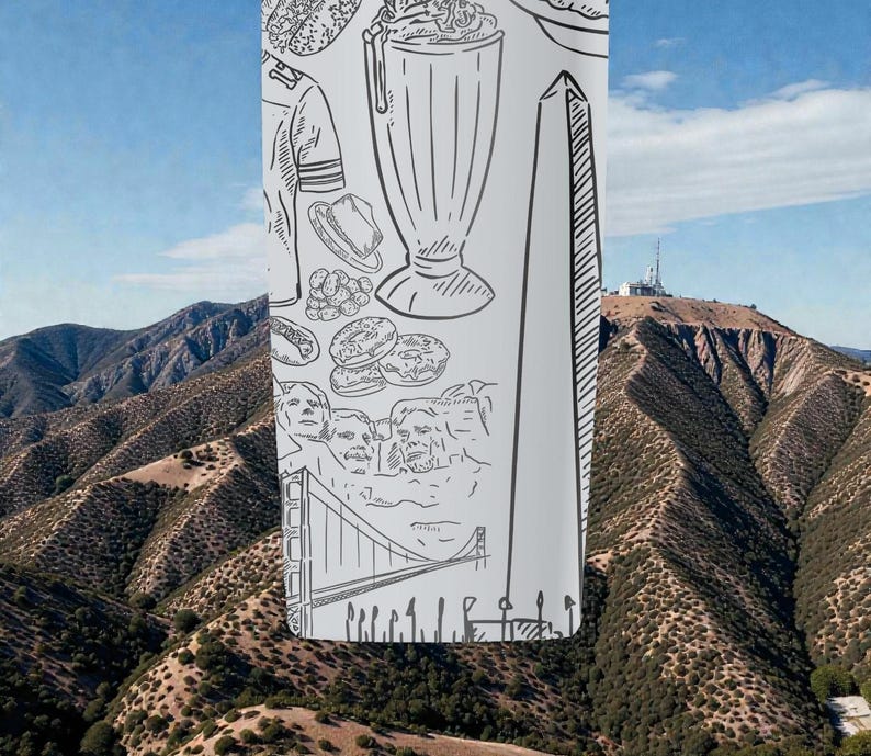 May include: A tall, white tumbler with black line drawings of American landmarks and food items, including a milkshake, donuts, and the Washington Monument. The background shows a mountain range under a blue sky.