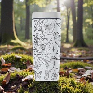 Puede incluir: Taza de viaje blanca con un dise&ntilde;o floral y colibr&iacute; en blanco y negro. El dise&ntilde;o incluye flores, mariposas y colibr&iacute;es. La taza es cil&iacute;ndrica y tiene una tapa blanca.