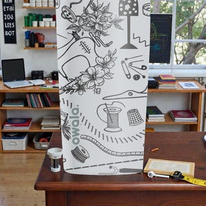 May include: A white fabric panel featuring a black and white illustration of sewing tools and floral elements. The design includes a sewing machine, measuring tape, and spools of thread. The word "owala" is printed on the fabric.