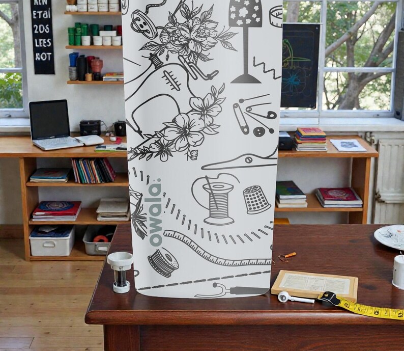 May include: A white fabric panel featuring a black and white illustration of sewing tools and floral elements. The design includes a sewing machine, measuring tape, and spools of thread. The word "owala" is printed on the fabric.