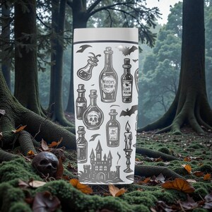 K&ouml;nnte beinhalten: Ein wei&szlig;er Reisebecher mit einer grauen Illustration von Zaubertr&auml;nken, einem Totenkopf, Flederm&auml;usen, einem Schloss und einer Kerze. Der Text "Witch's Brew" und "Love Potion" sind ebenfalls abgebildet. Der Becher steht vor einem Waldhintergrund.