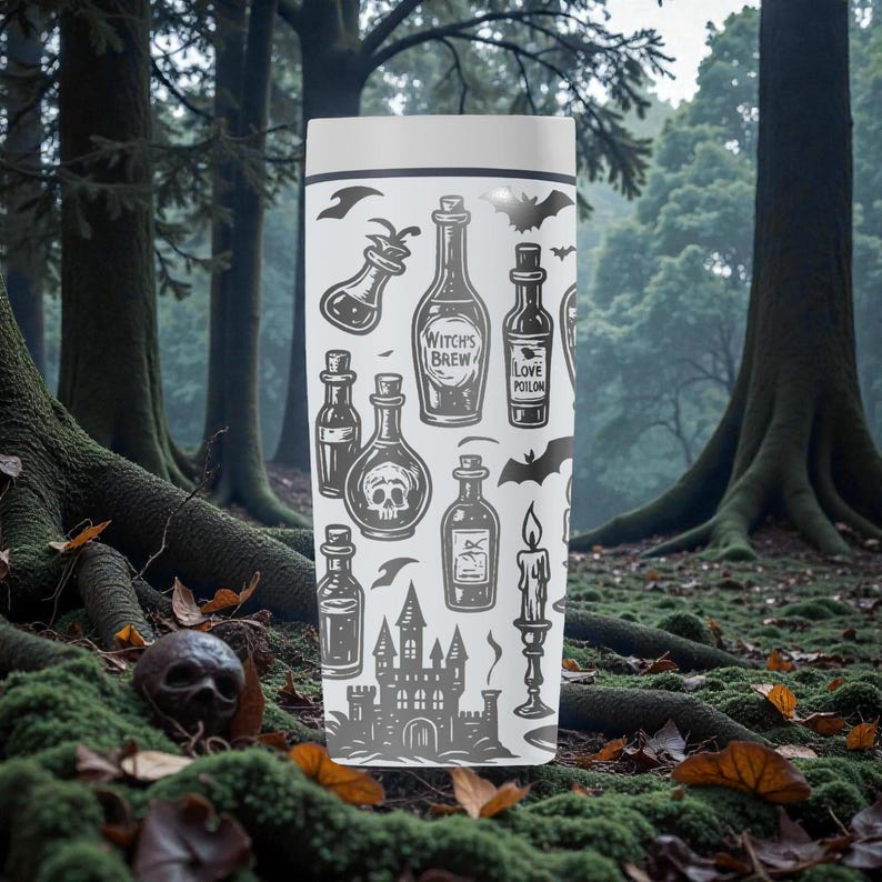 K&ouml;nnte beinhalten: Ein wei&szlig;er Reisebecher mit einer grauen Illustration von Zaubertr&auml;nken, einem Totenkopf, Flederm&auml;usen, einem Schloss und einer Kerze. Der Text "Witch's Brew" und "Love Potion" sind ebenfalls abgebildet. Der Becher steht vor einem Waldhintergrund.