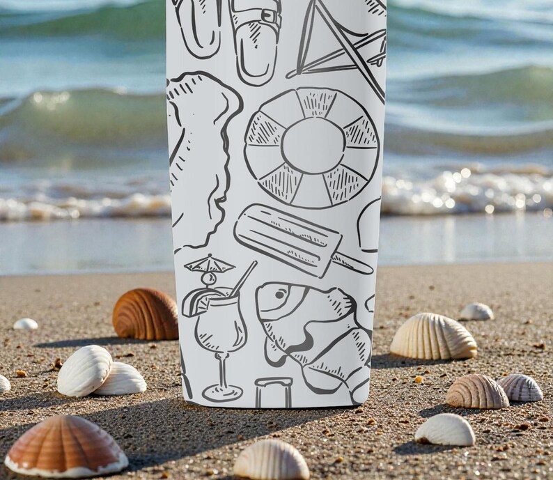 Op de afbeelding: Een witte beker met een zwarte lijntekening van strandthema's, waaronder een reddingsboei, een ijsje en een vis. De beker staat op een zandstrand met schelpen.