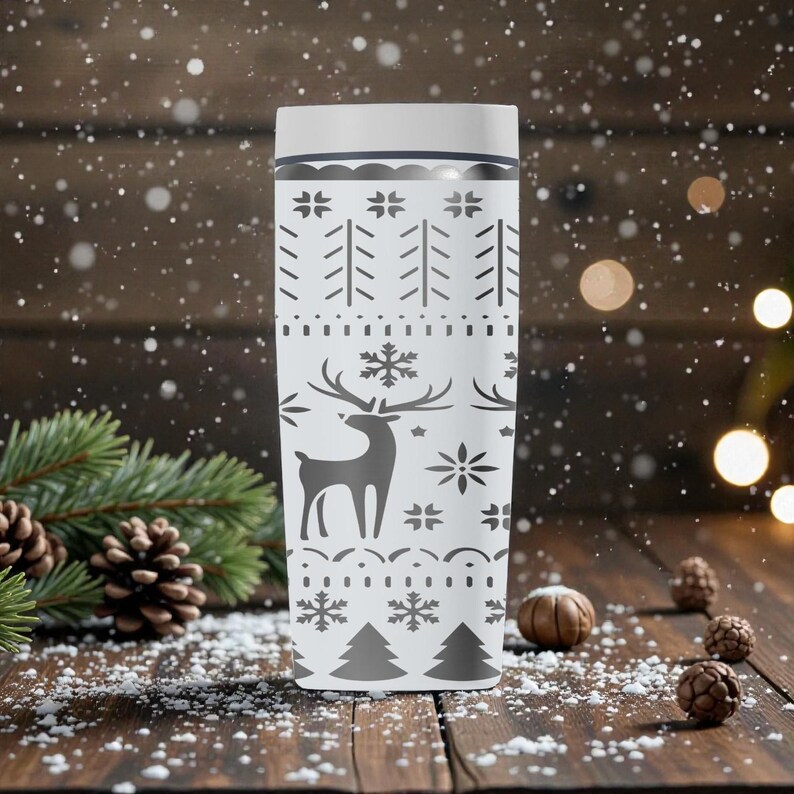 May include: A white travel mug with a festive winter design. The mug features a pattern of trees, snowflakes, and a reindeer silhouette in gray. The mug is cylindrical and has a white lid.