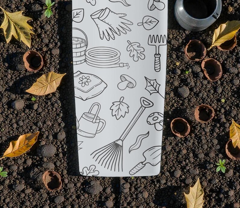 Puede incluir: Una toalla blanca con tem&aacute;tica de jard&iacute;n con ilustraciones en negro de herramientas y elementos de jardiner&iacute;a, incluyendo una regadera, un rastrillo, guantes y hojas. La toalla est&aacute; rodeada de tierra, hojas y c&aacute;scaras de nueces.