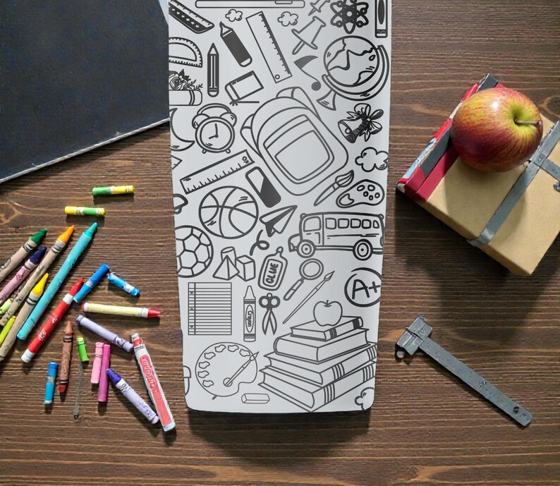 May include: A white tumbler with a black school-themed doodle design sits on a wooden surface, surrounded by crayons, a chalkboard, a wrapped gift, an apple, and a metal ruler. The tumbler features illustrations of school supplies.