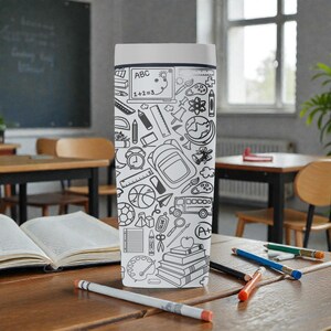 May include: A white and gray travel mug with a school-themed doodle design. The design includes images of a laptop, ruler, backpack, books, and other school supplies. The mug is sitting on a wooden desk with pencils and an open book.