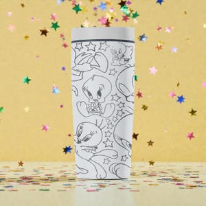 May include: A white tumbler featuring a repeating black and white cartoon graphic of Tweety Bird and stars. The tumbler has a white lid and a cylindrical shape. The background is a gold color with scattered star-shaped confetti.