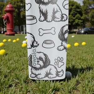 May include: A white water bottle with a black and white dog-themed pattern. The design includes illustrations of dogs, paw prints, dog bowls, and bones. The word "owala" is printed on the bottle.