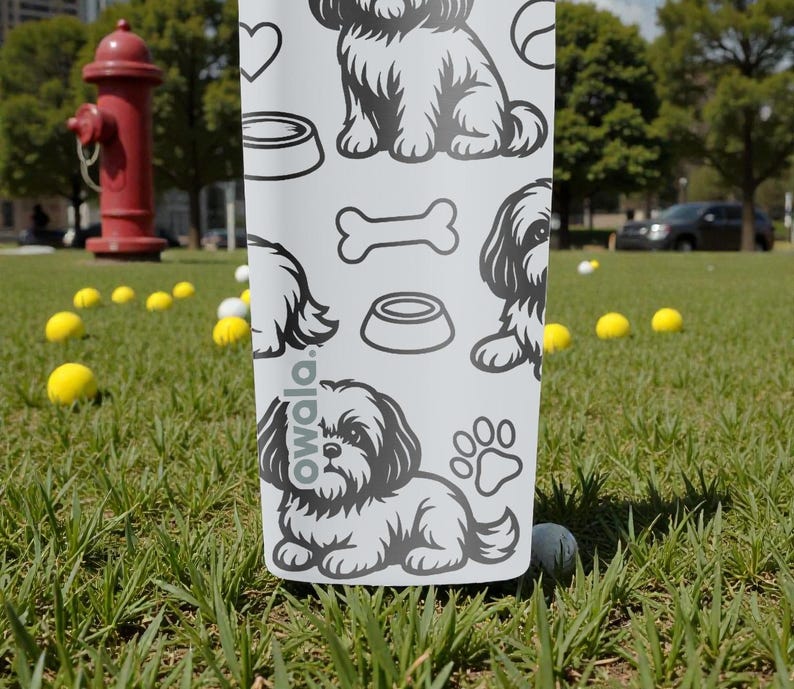 May include: A white water bottle with a black and white dog-themed pattern. The design includes illustrations of dogs, paw prints, dog bowls, and bones. The word "owala" is printed on the bottle.