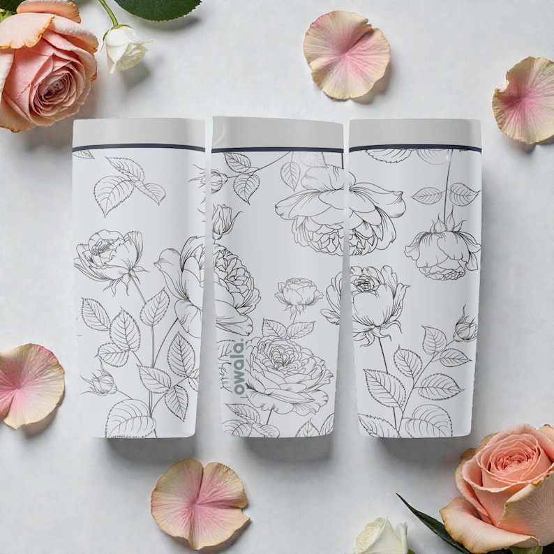 Op de afbeelding: Drie witte waterflessen met een bloemenrozenontwerp. De flessen hebben een grijze bovenkant en zijn versierd met zwarte lijntekeningen van rozen en bladeren. Het woord "owala" staat op de zijkant van een fles. Roze rozenblaadjes en rozen zijn rond de flessen verspreid.